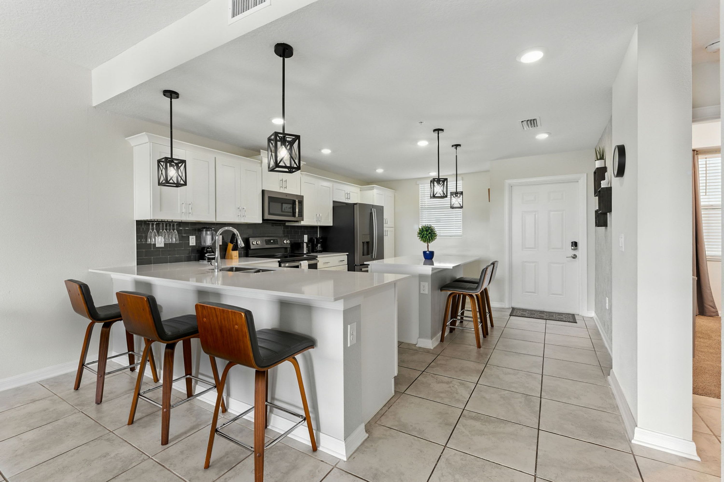 A modern kitchen with white cabinetry, a large island with bar stools, stainless steel appliances, and pendant lighting.
