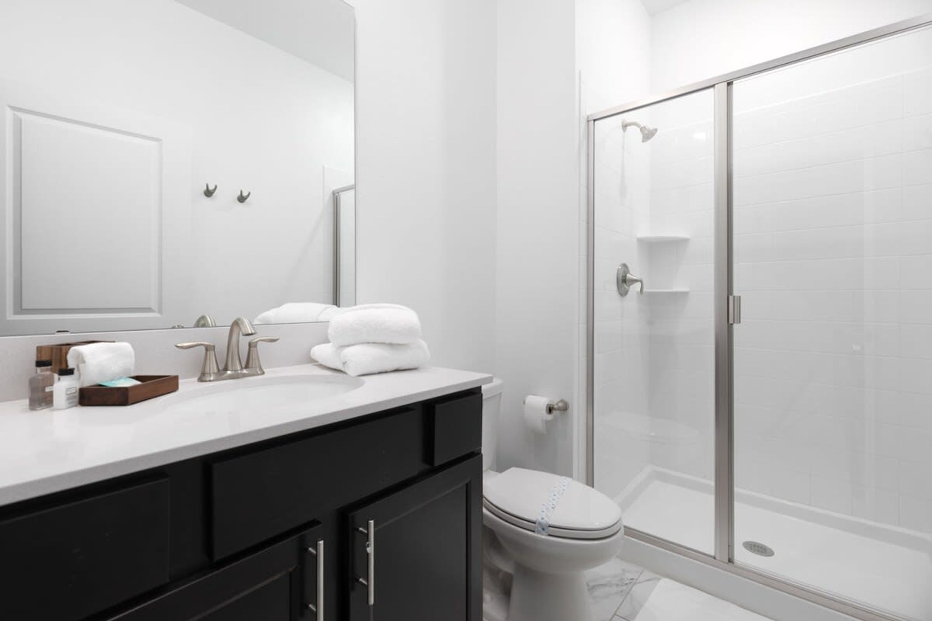Ein modernes Badezimmer mit einem weißen Waschbecken, schwarzen Schränken, einem großen Spiegel und einer Duschkabine aus Glas.
