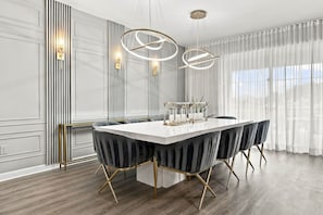 A modern dining area with a large rectangular table, upholstered chairs, and pendant lighting. - Themed 9BR Retreat, Pool & Soccer Fun (Kissimmee)