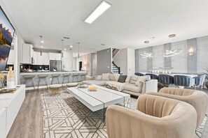 A modern living room with a white sofa, beige armchairs, and a coffee table. - Themed 9BR Retreat, Pool & Soccer Fun (Kissimmee)