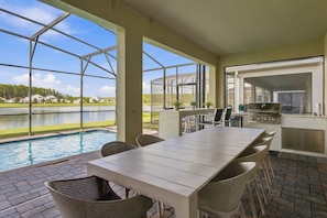 A covered outdoor area with a pool, a dining table, chairs, and a grill. - Themed 9BR Retreat, Pool & Soccer Fun (Kissimmee)