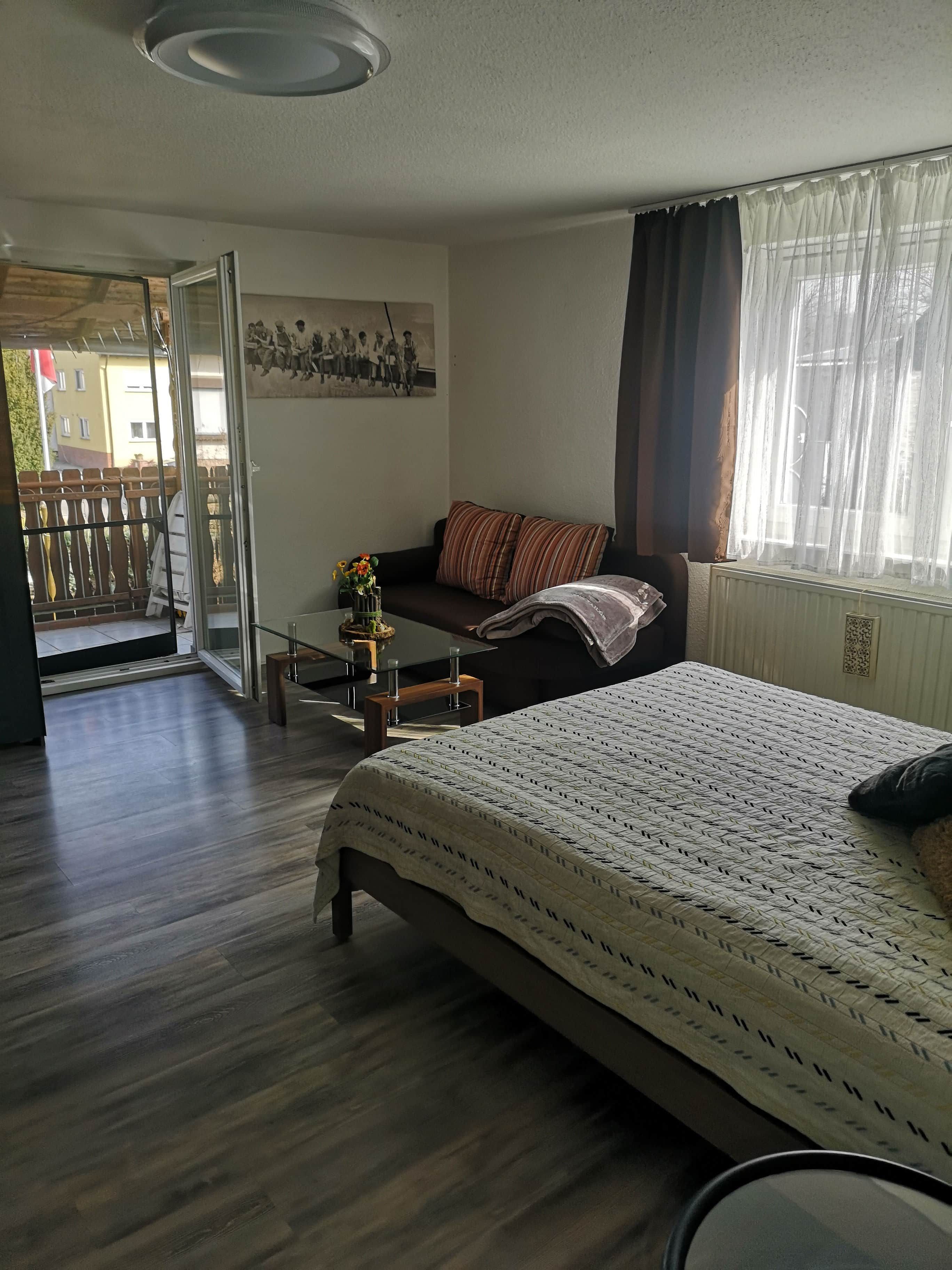 A bedroom with a bed, a sofa, a small table with a vase, and a window with curtains.