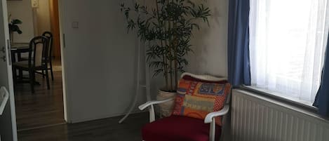 Une pièce comprenant un lit, une chaise, une plante en pot, une fenêtre avec des rideaux et un radiateur.