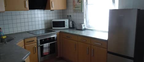 Een keuken met houten kastjes, een magnetron, een broodrooster, een fornuis en een koelkast.