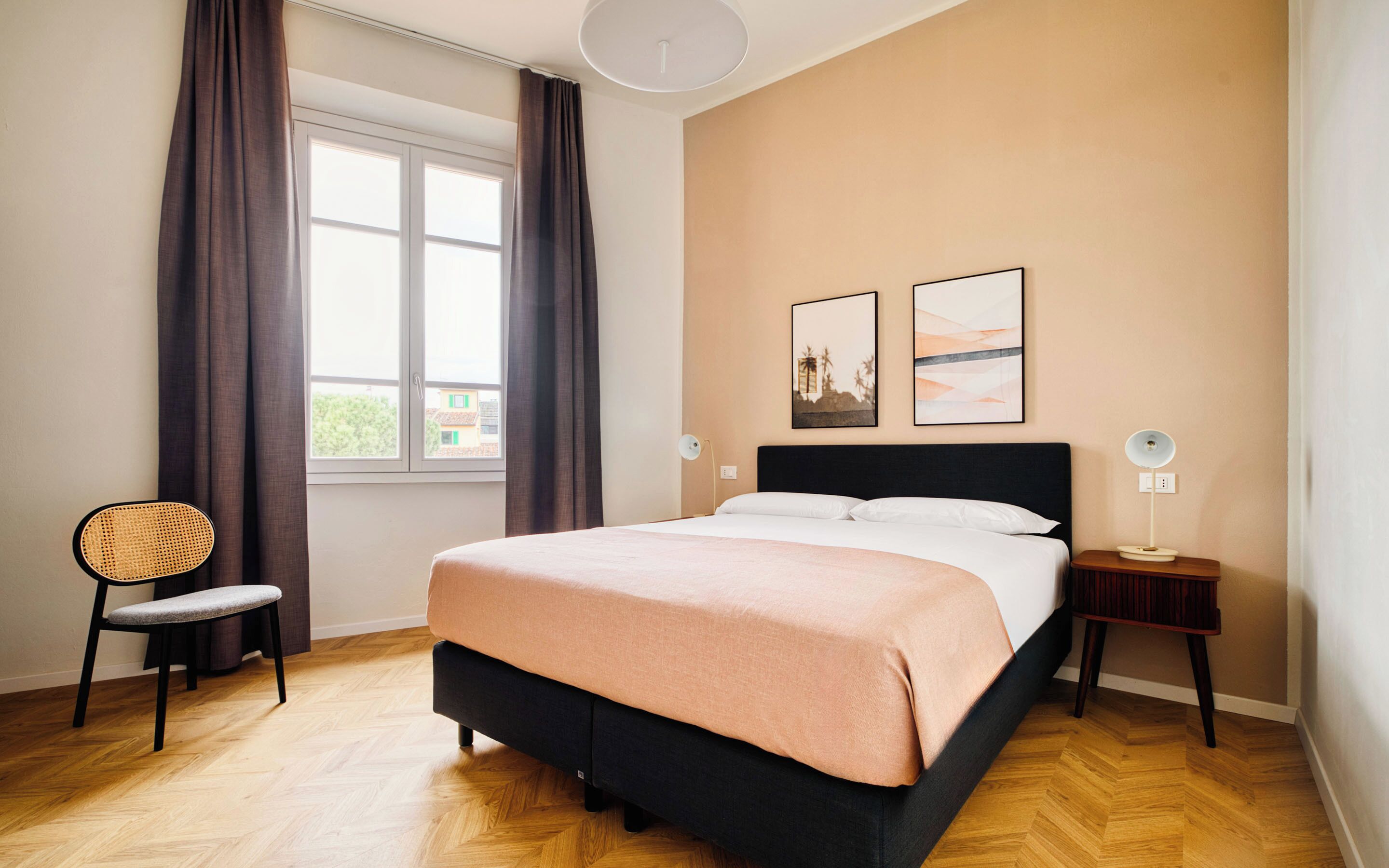 A bedroom with a bed, a chair, a nightstand, a lamp, and two wall art pieces.
