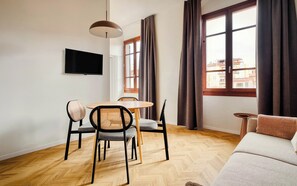 A modern living room with a wooden herringbone floor, a round wooden table with four chairs, a flat-screen TV mounted on the wall, and a sofa with a throw pillow. - Limehome Florence Via Guelfa (Florence)