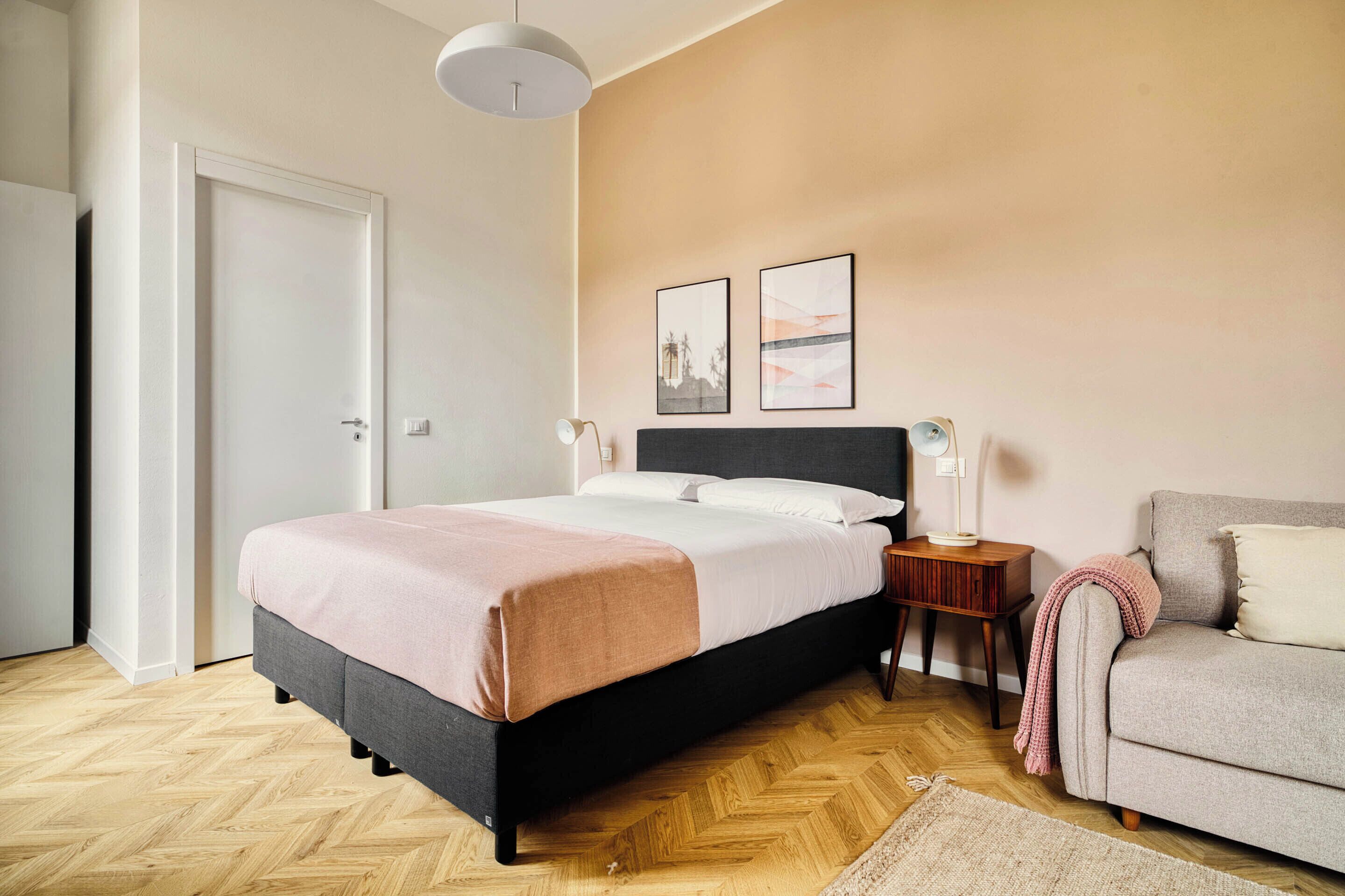 A bedroom with a bed, bedside table, lamp, and a sofa.