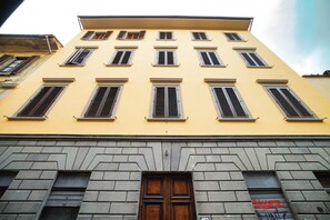 A multi-story building with a yellow facade, multiple windows with shutters, and a central wooden door. - Limehome Florence Via Guelfa (Florence)