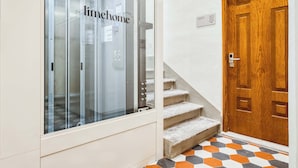 A hallway with a glass elevator, a wooden door, and a staircase with a patterned floor. - Limehome Florence Via Guelfa (Florence)