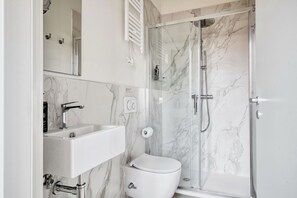 A bathroom with a marble sink, toilet, and a glass-enclosed shower. - Limehome Florence Via Guelfa (Florence)