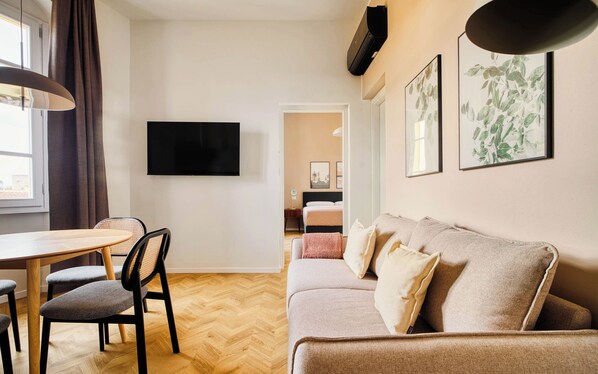A modern living room with a wooden herringbone floor, a sofa, a dining table with chairs, a flat-screen TV, and framed botanical prints on the wall. - Limehome Florence Via Guelfa (Florence)