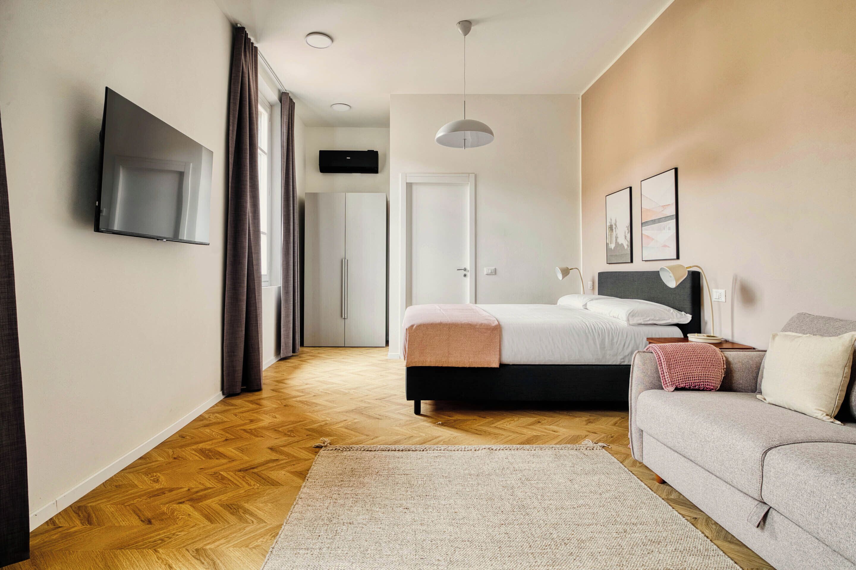 Quarto de hotel moderno com uma cama, um sofá, uma televisão e um corredor que leva a um banheiro.