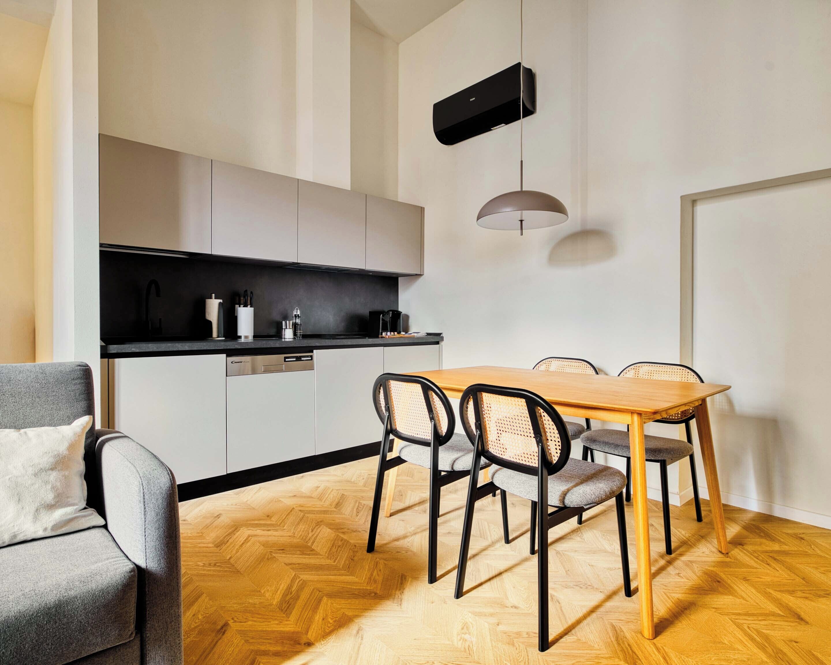 A modern kitchen with a dining area, including a wooden herringbone floor, a dining table with chairs, and a pendant light.