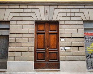 Puerta doble de madera con el número '85' arriba, integrada en un edificio de fachada de ladrillo.