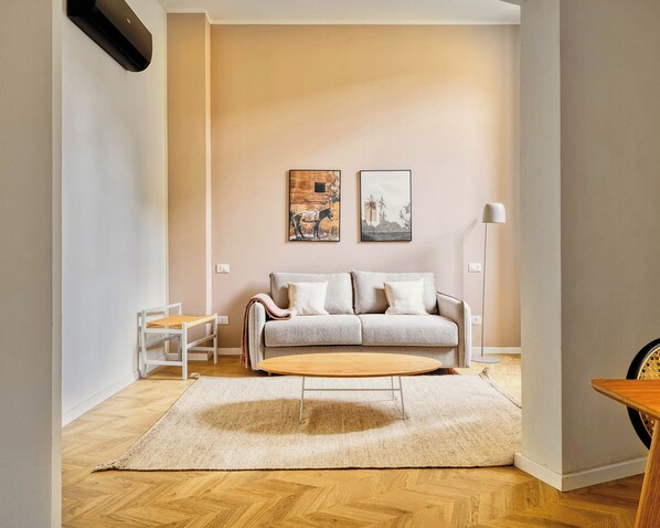 A living room with a sofa, two wall-mounted pictures, a standing lamp, and a wooden coffee table. - Limehome Florence Via Guelfa (Florence)