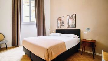 A bedroom with a bed, a chair, a bedside table, and two wall-mounted pictures.