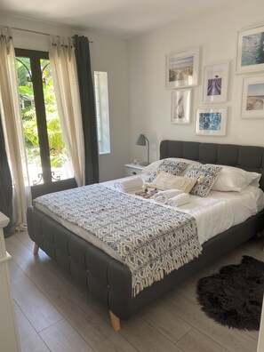 Une chambre à coucher avec un grand lit, une table de chevet, une lampe et une fenêtre avec des rideaux.