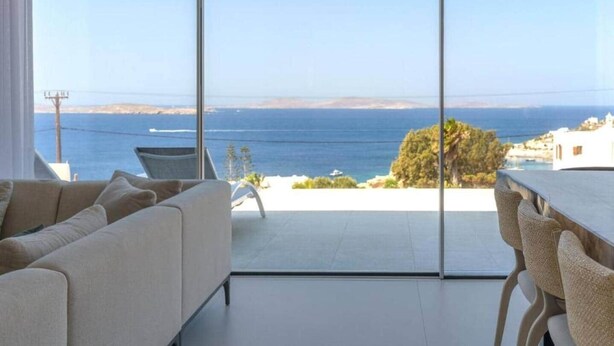 Un saló modern amb una gran porta de vidre que dona a un balcó amb vista al mar.