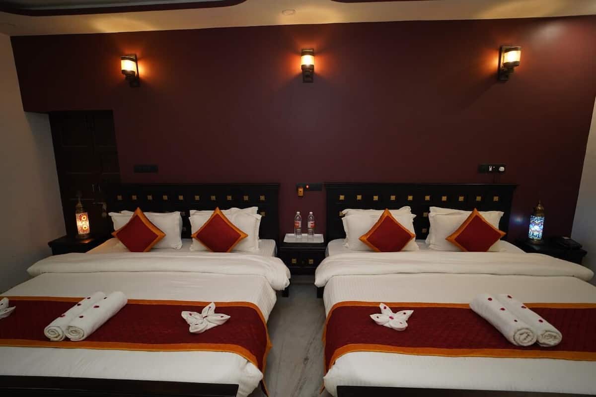 Habitación de hotel con dos camas, cada una con ropa blanca y detalles rojos, y lámparas fijadas a la pared.