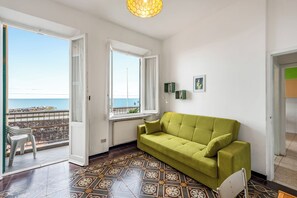 Une pièce avec un canapé vert, un sol à motifs, une vue sur la mer et un balcon avec des chaises.