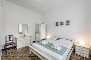 Une chambre à coucher comprenant un lit, des tables de chevet, une commode, une chaise, un miroir et une porte.