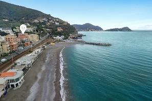 A coastal town with a beach, buildings, and a rocky outcrop in the water.