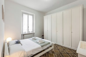A bedroom with a bed, a wardrobe, a radiator, and a window.
