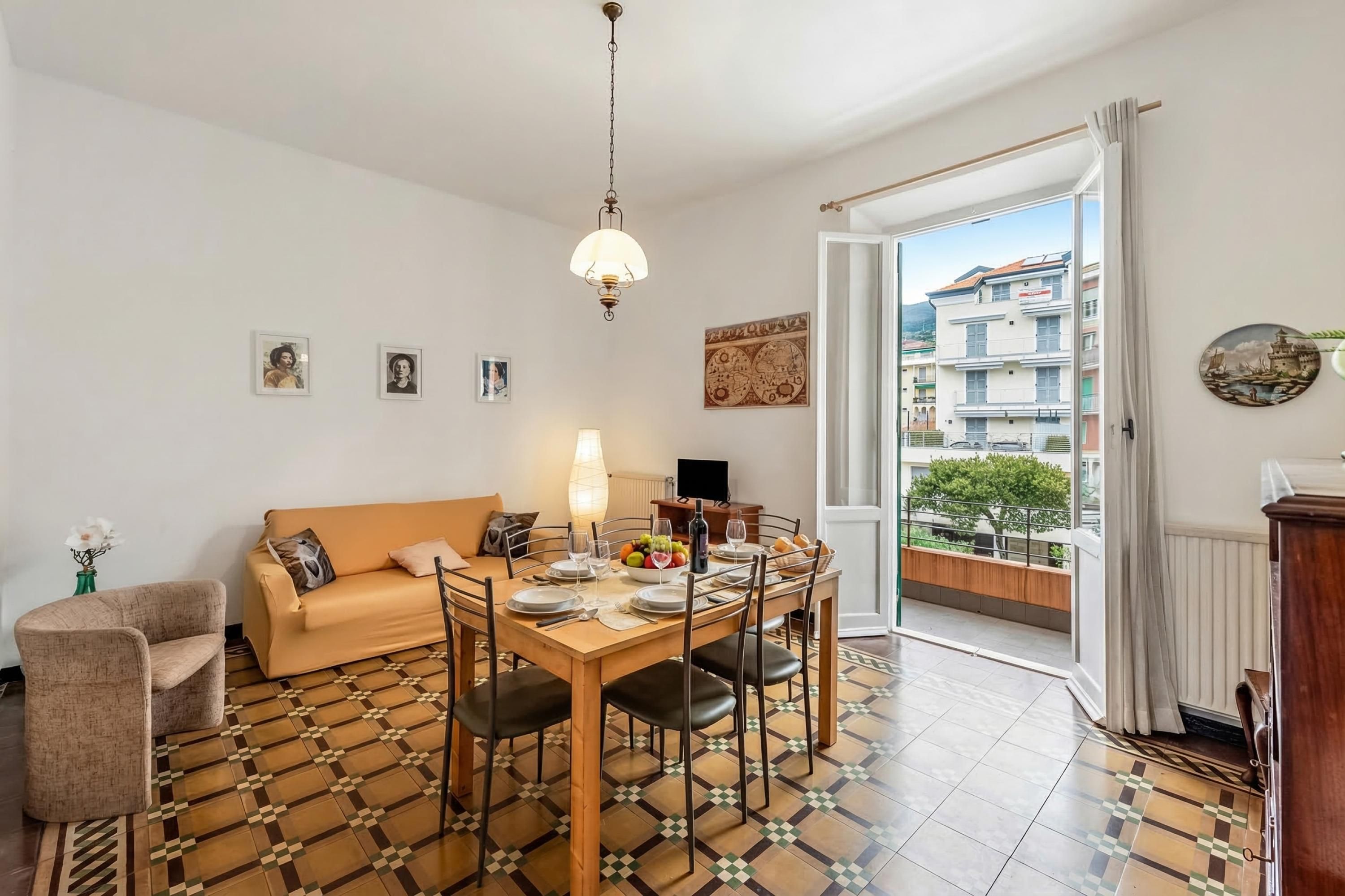 Un comedor con una mesa dispuesta para cuatro personas, un sofá y vistas a un edificio por una puerta abierta.