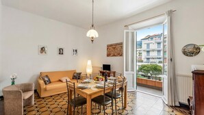 A dining area with a table set for four, a sofa, and a view of a building through an open door. - Amiado Apartment With Sea View Balcony (Lavagna)