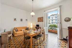 A dining area with a table set for four, a sofa, and a view of a building through an open door. - Amiado Apartment With Sea View Balcony (Lavagna)
