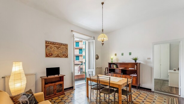 A living room with a sofa, TV, lamp, dining table, chairs, and a patterned floor. - Amiado Apartment With Sea View Balcony (Lavagna)