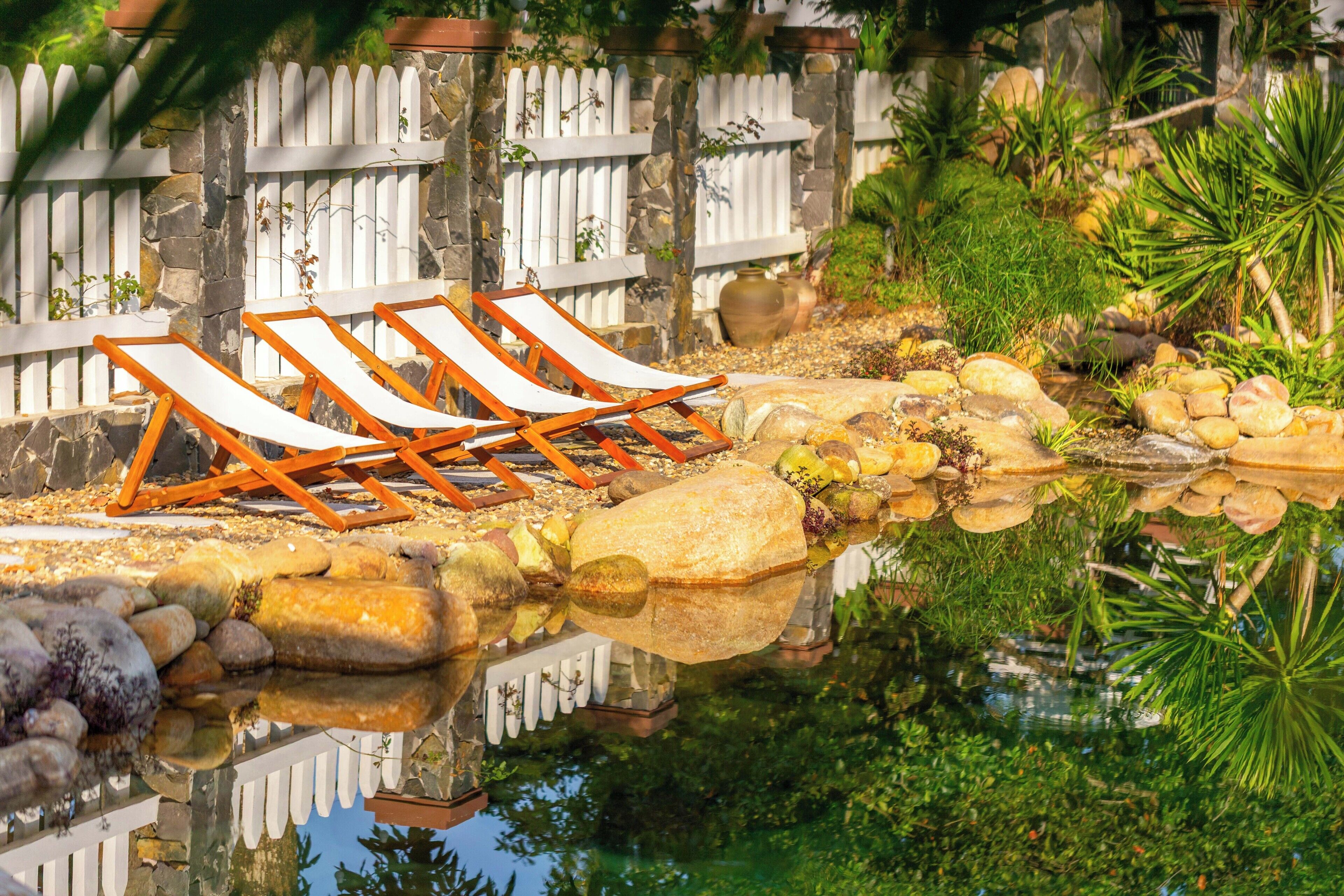 A poolside area with lounge chairs, a stone wall, and a white picket fence.