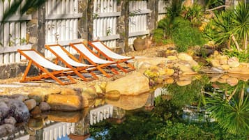 A poolside area with lounge chairs, a stone wall, and a white picket fence.