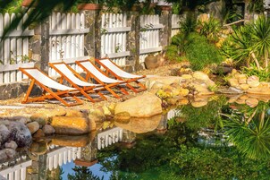 Un área junto a la piscina con sillones de descanso, un muro de piedra y una cerca de piquetes blancos.