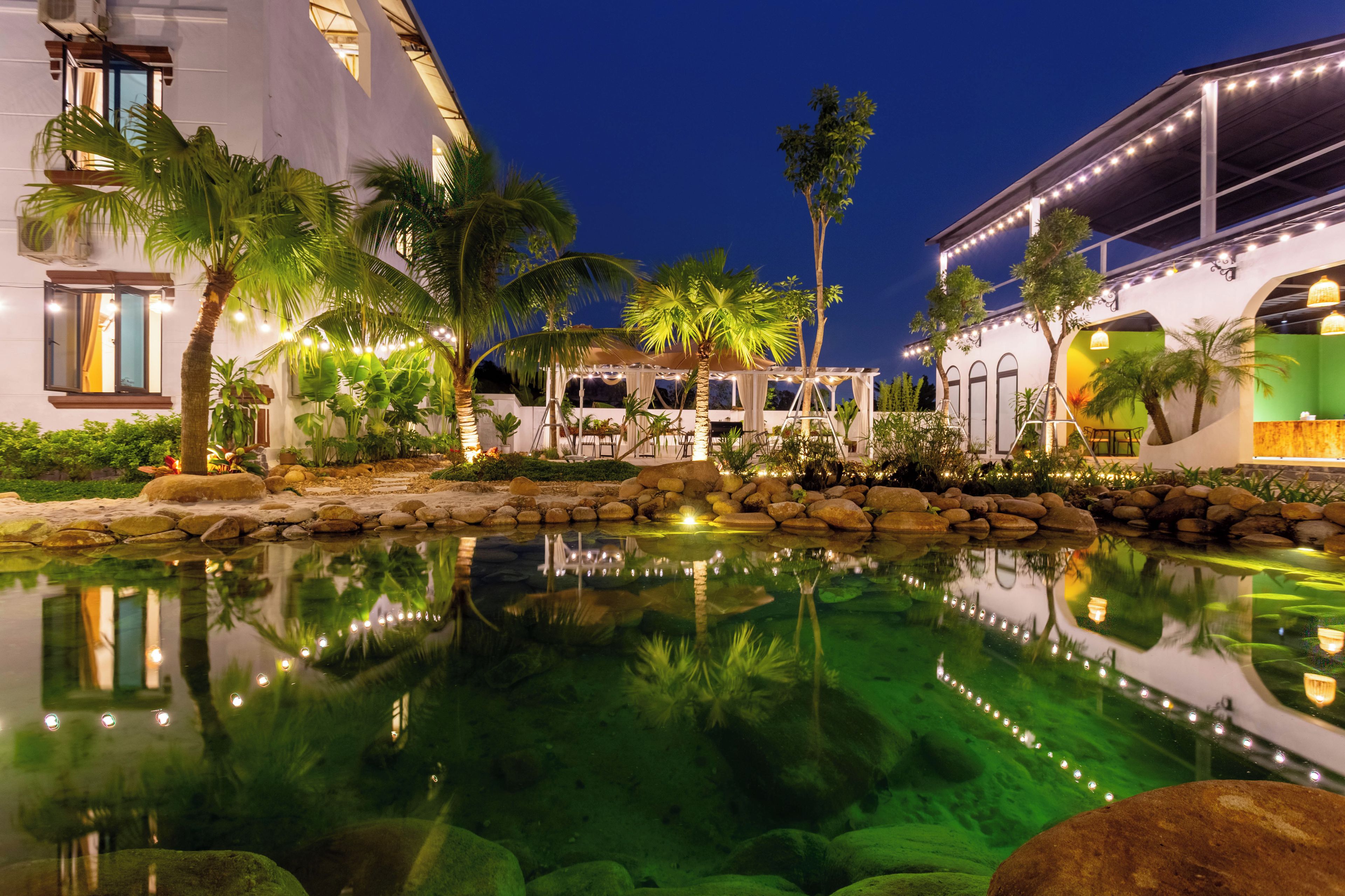 A nighttime view of a hotel courtyard with a reflective pool, palm trees, and a covered seating area.