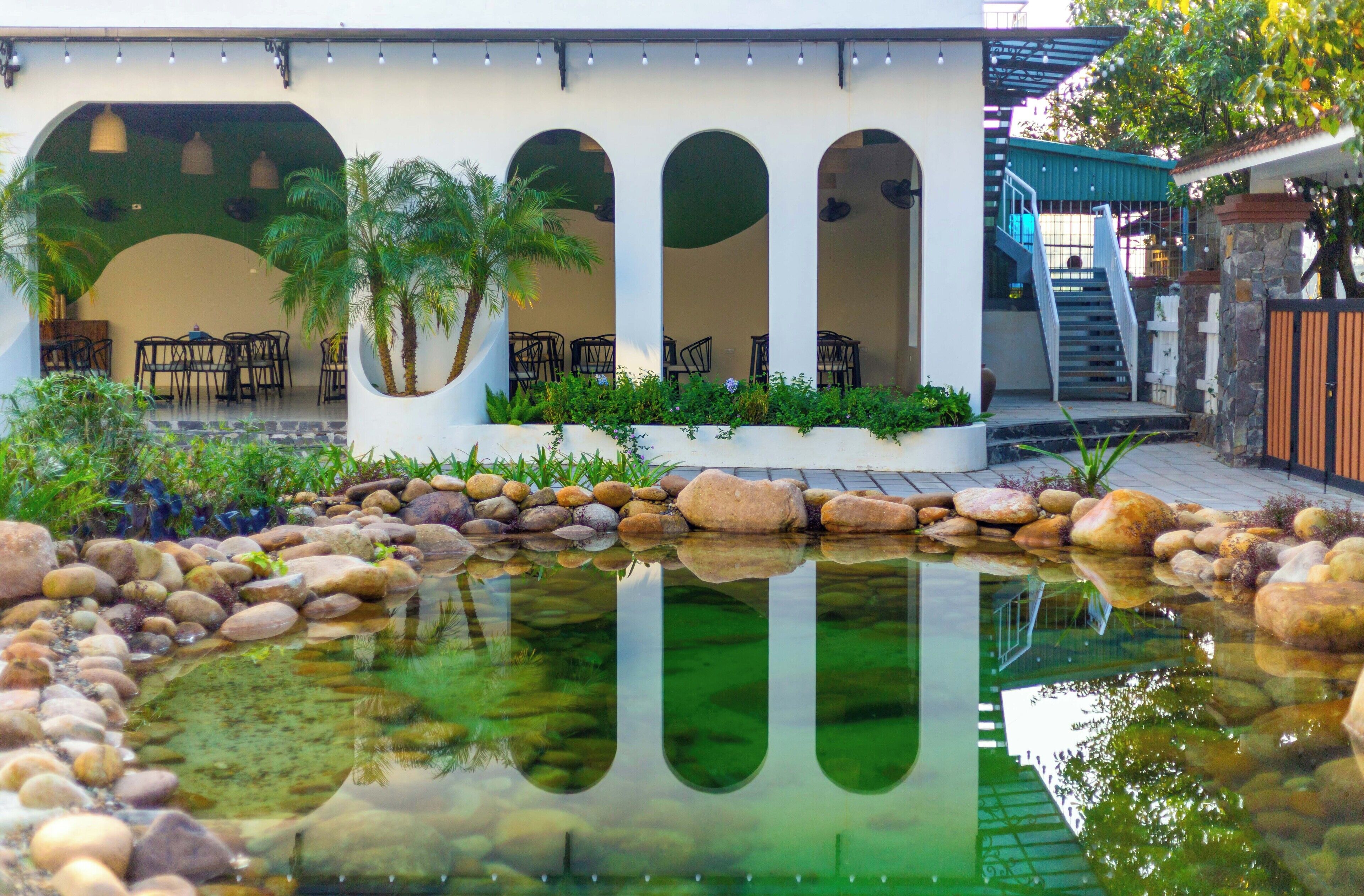 Un patio con un estanque reflectante, un espacio de descanso y una escalera que lleva a una zona cubierta.