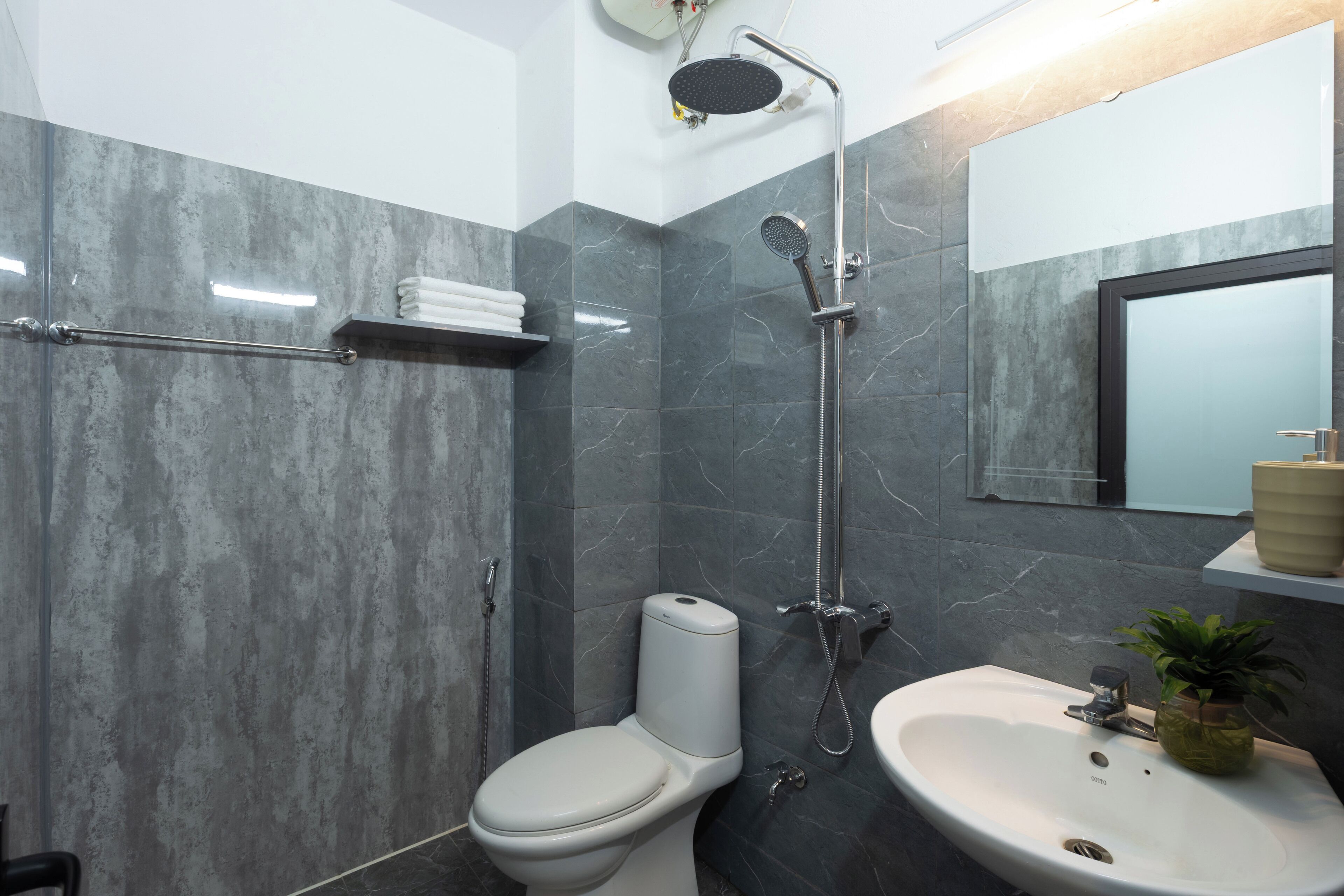 A modern bathroom with a toilet, shower, sink, and marble walls.