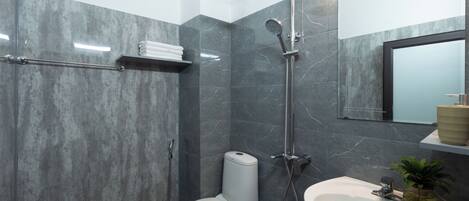 A modern bathroom with a toilet, shower, sink, and marble walls.