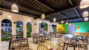 A restaurant with multiple tables and chairs, a green wall, and a view of a building outside. - Sol Flow Retreat (Hoa Lu)