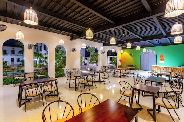 A restaurant with multiple tables and chairs, a green wall, and a view of a building outside. - Sol Flow Retreat (Hoa Lu)