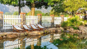 Uma área de piscina ao ar livre tranquila, com espreguiçadeiras, cerca branca e um muro de pedra.