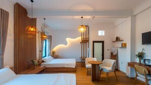 Quarto de hotel moderno com duas camas, área de estar com mesa e cadeiras, e um detalhe decorativo na parede.