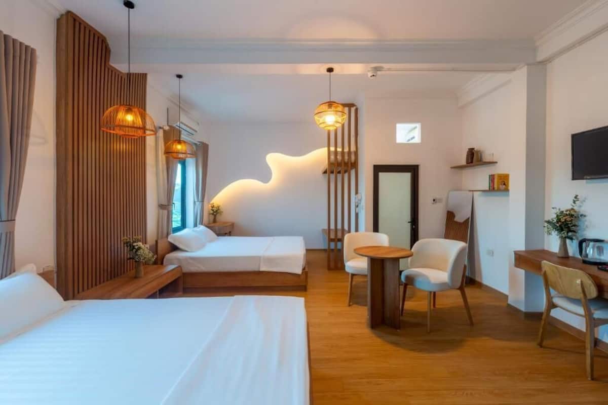 Una habitación de hotel moderna con dos camas, una zona de estar con una mesa y sillas, y un elemento decorativo en la pared.