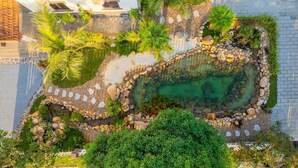 An aerial view of a landscaped area with a swimming pool, surrounded by rocks and greenery, including palm trees and shrubs. - Sol Flow Retreat (Hoa Lu)