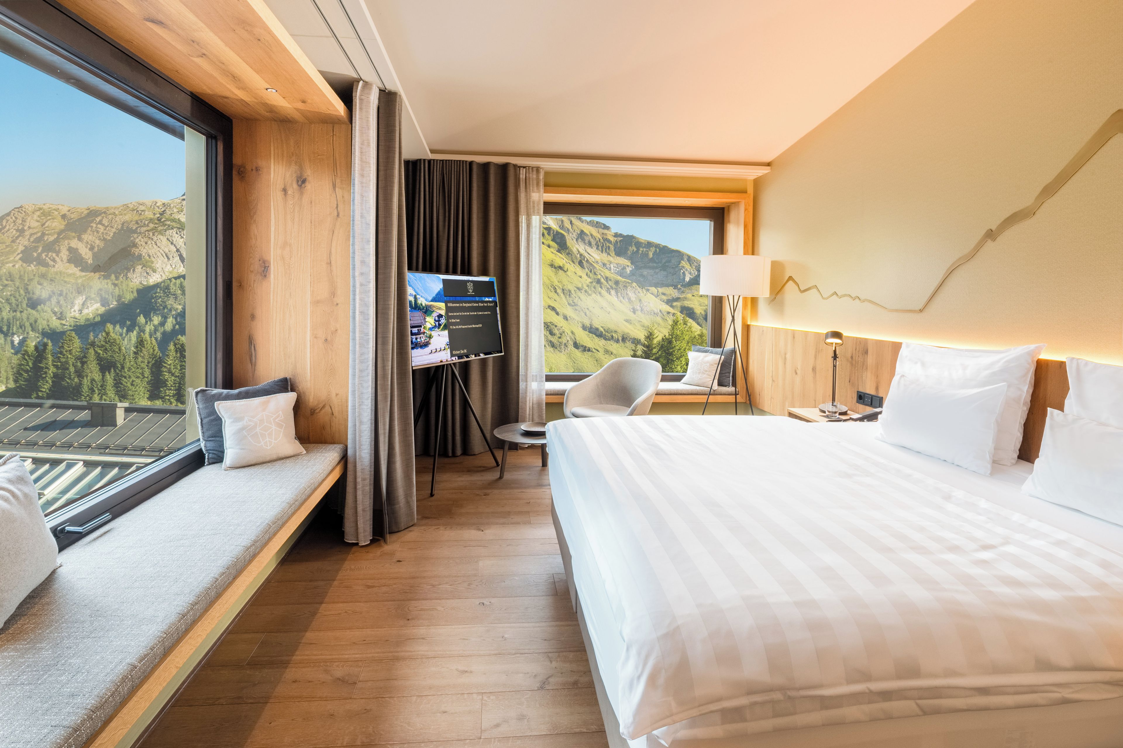 Habitación de hotel con cama, escritorio, silla, televisor y vistas a montañas.