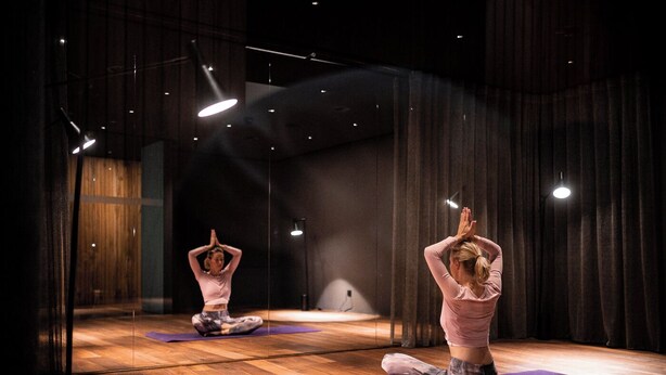 Una sala yoga con pavimento in legno, tappetini viola e uno specchio grande.