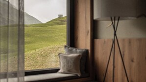 Una stanza con una finestra che si affaccia su un paesaggio erboso, un comodino e una lampada da terra.