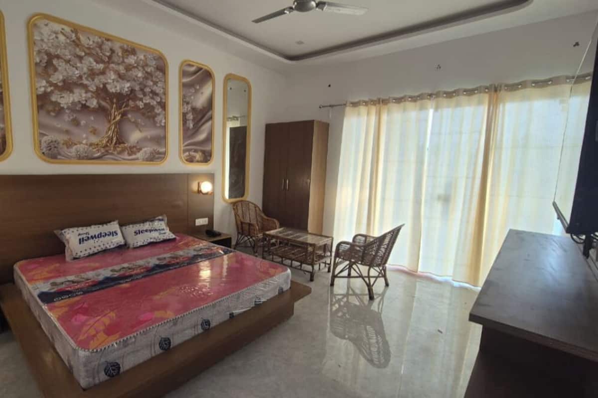 A bedroom with a large bed, a desk, and a chair. There are wall-mounted lights and a ceiling fan.