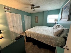 A bedroom with a bed, a desk with a computer, a ceiling fan, and a window with blinds. - Beach   Pool Open  Direct Beachfront Condo  Sunsets (Siesta Key)
