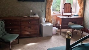 Een hotelkamer met een grote flatscreen televisie aan de muur, een houten bureau met stoel, een klein wit tafeltje en een groene fauteuil.